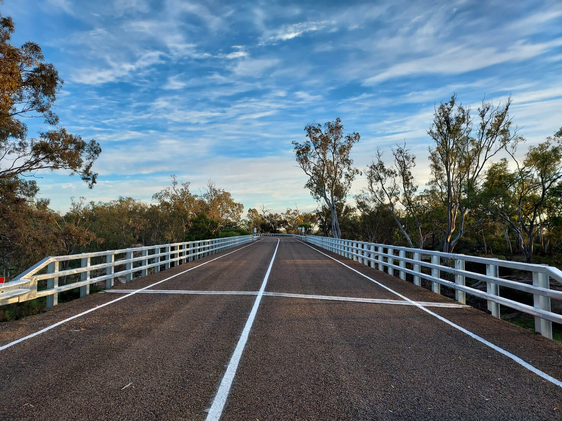 Looking down the road over a wide new bridge. Surrounded by gum trees and a blue sky.