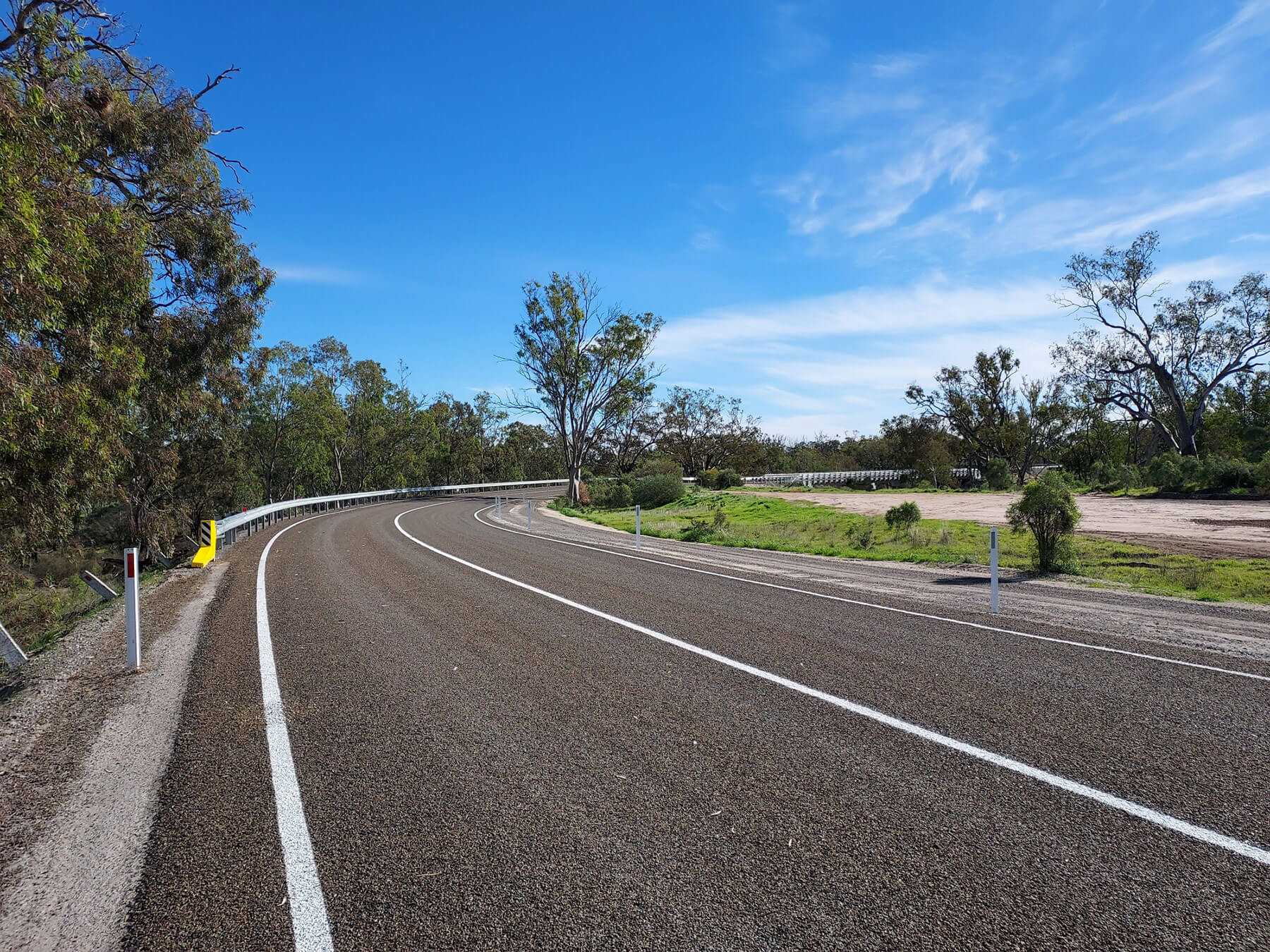 Chris-obrien-ALBACUTYA-BRIDGE-3 Photo of a wide, new regional road curing off to the right, surrounded by trees and a blue sky.