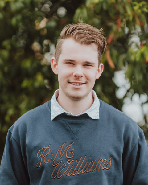 Chris-obrien-team-JackDownes2 Photo of Jack Downes wearing a dark blue jumper standing infront of green trees.