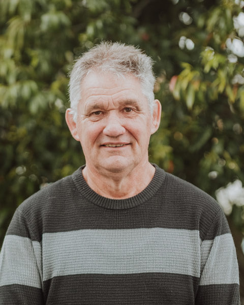 Chris-obrien-team-andrewpowell Photo of Andrew Powell wearing a green and grey striped jumper standing infront of green trees.