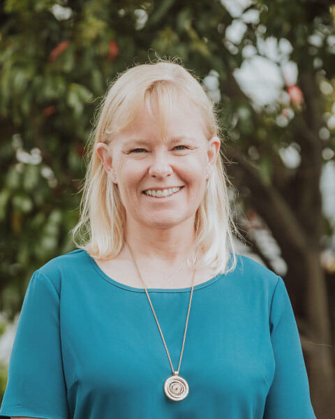 Chris-obrien-team-sallydownes Photo of Sally Downes wearing a teal blue top standing infront of green trees.