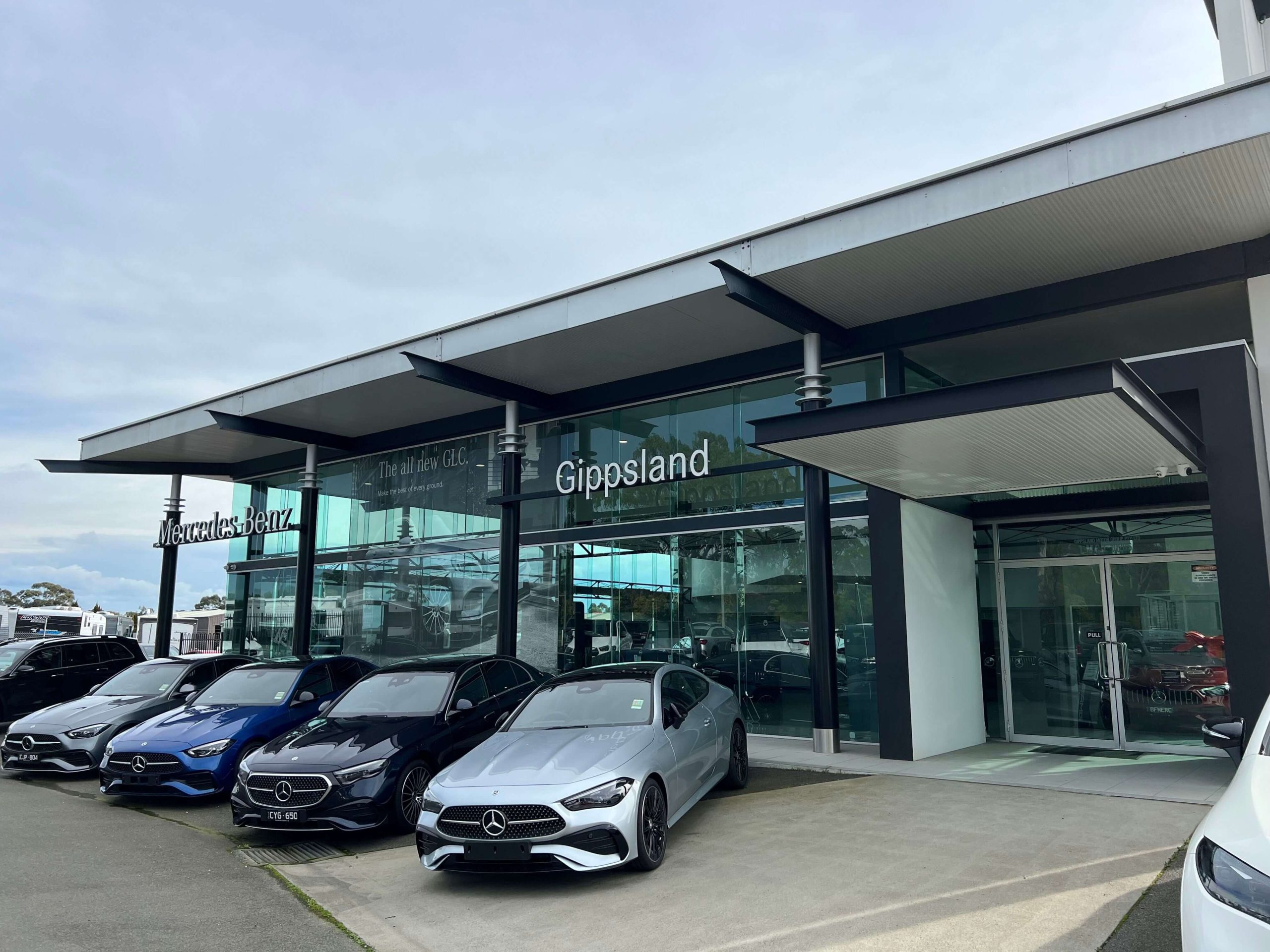 Photo of a car dealership glass showroom for Mercedes-Benz, and four Mercedes sports cars parked infront of the building.