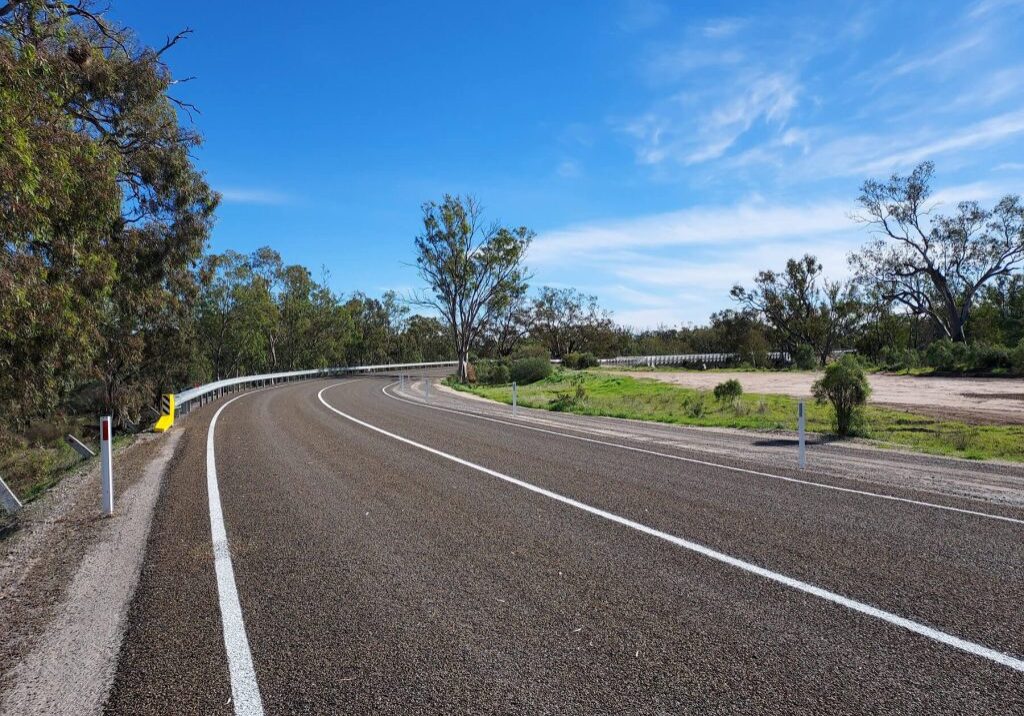 Photo of a wide, new regional road curing off to the right, surrounded by trees and a blue sky.
