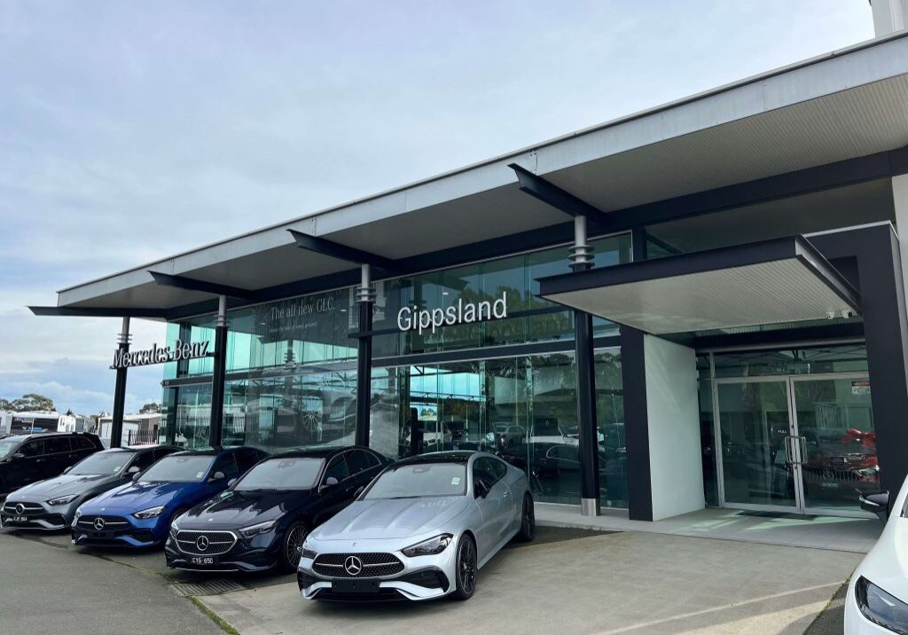Photo of a car dealership glass showroom for Mercedes-Benz, and four Mercedes sports cars parked infront of the building.